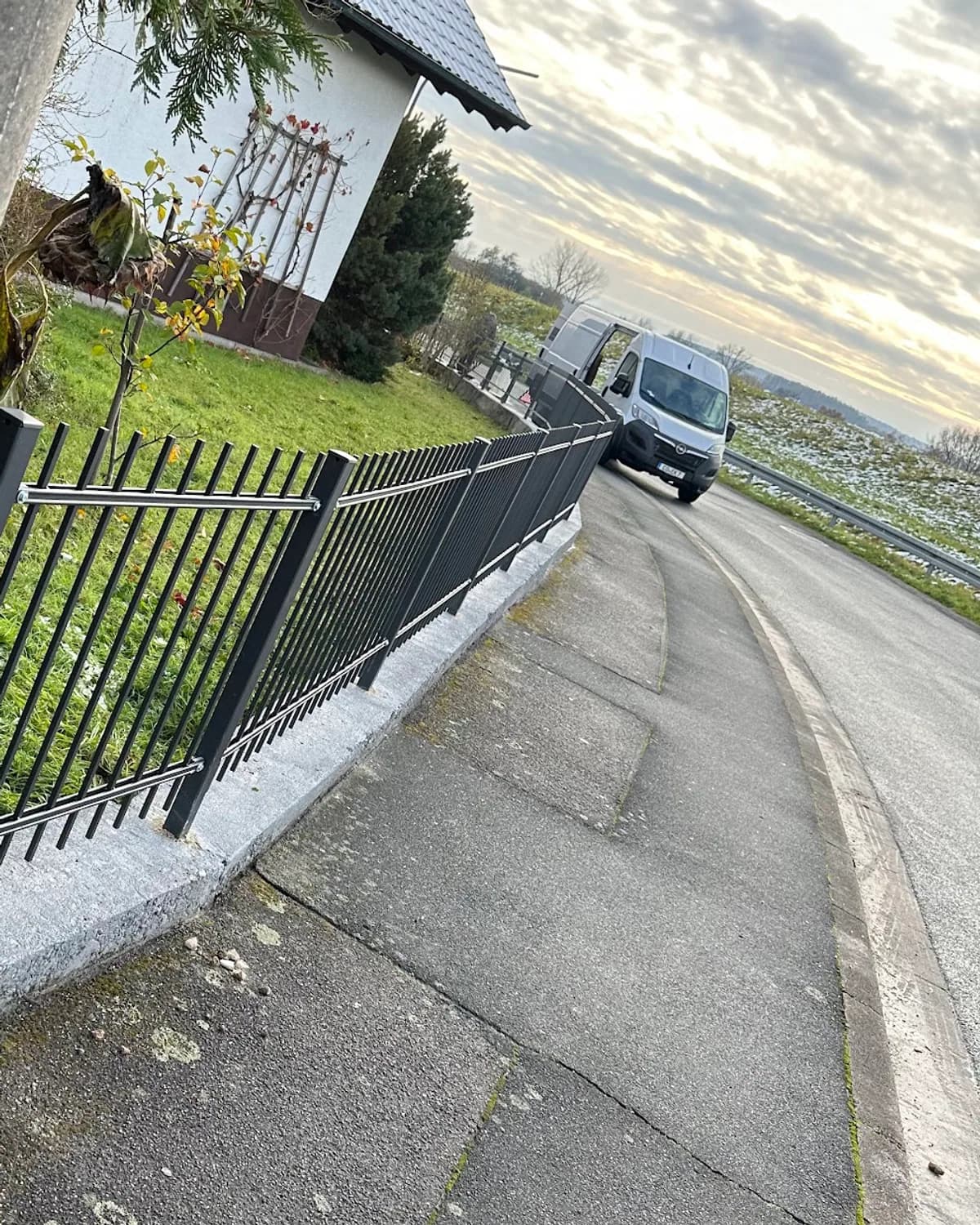 Metallzaun mit senkrechten Stäben an einer Grundstücksgrenze am Straßenrand im Abendlicht